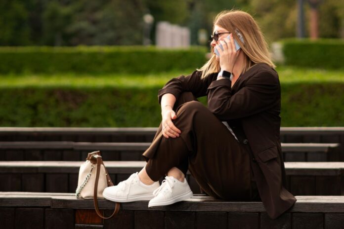 Woman sitting on bench, wearing brown suit and talking on the phone. Κομψότητα χωρίς τακούνι; Κι όμως, με τα γυναικεία sneakers γίνεται